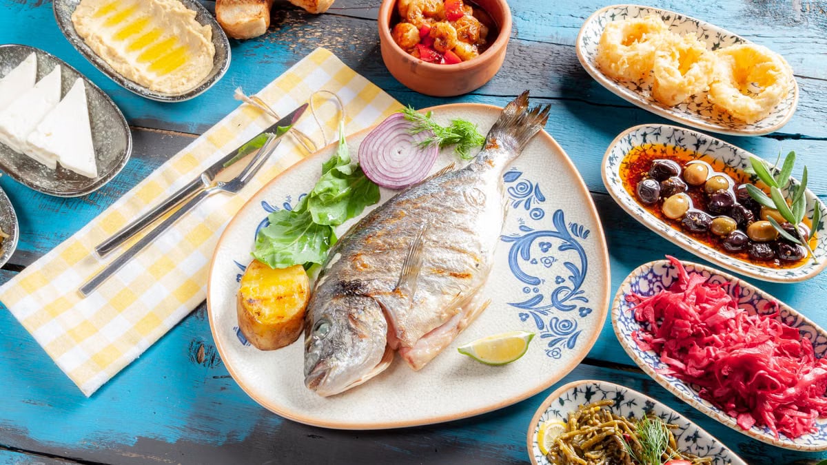 A vibrant Mediterranean meal featuring grilled fish and assorted appetizers on a rustic table.
