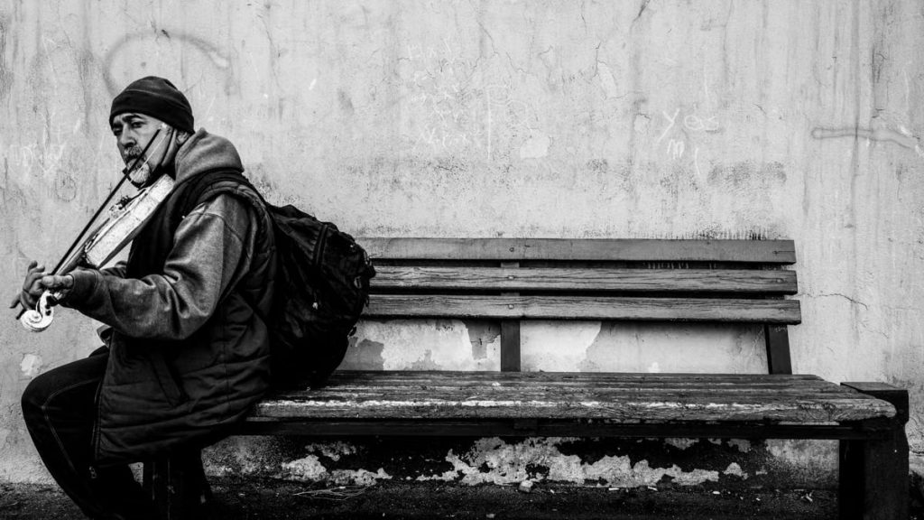 An elderly street musician plays the violin on a bench in Tehran, Iran, captured in black and white.
